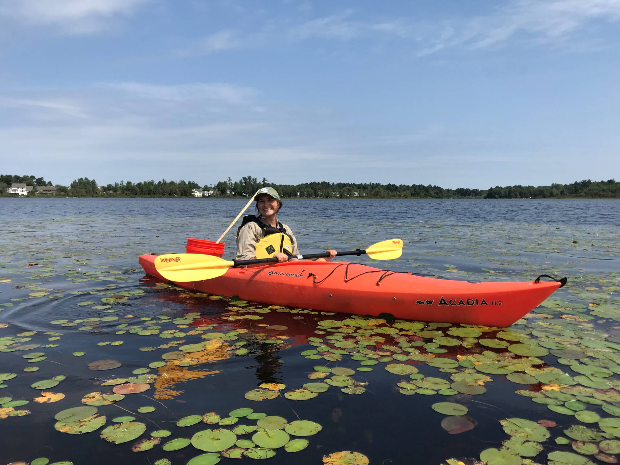 Kate Lucas poses for a photo while paddling an orange kayak through lily pads on a lake.